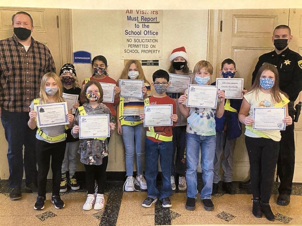 Deputy Espel and Principal Stein stand in the lobby with 10 students wearing green safety belts and holding certificates