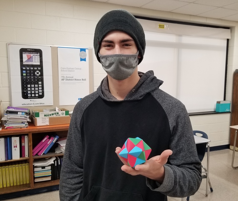 high school male wearing a black knit hat and holding a colorful origami sphere