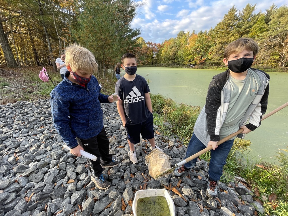 three middle school boys by a pond with a net and bucket