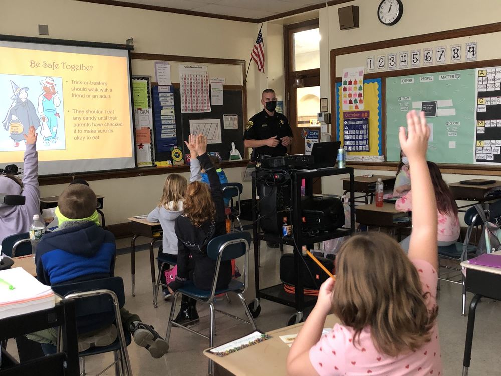 Deputy Espel at the front of a classroom and seated elementary students with hands raised