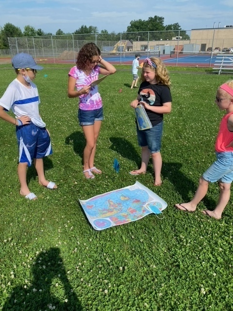 four middle school students outside looking at a map laid on the grass