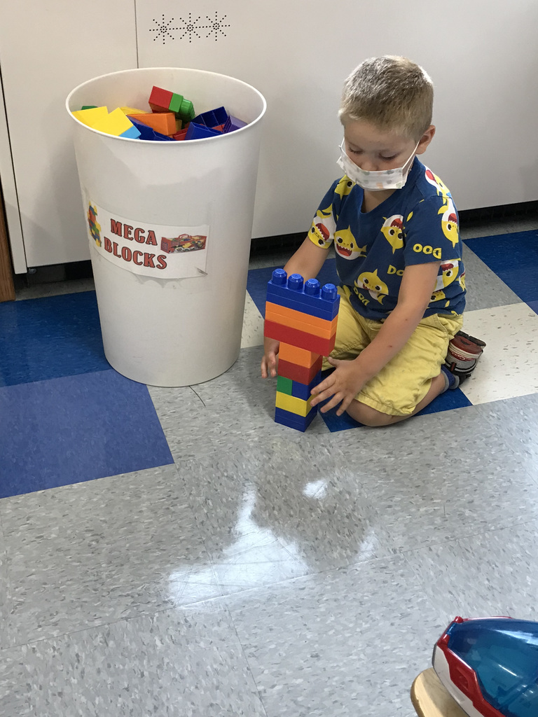 pre-kindergarten boy kneels on the classroom floor and plays with plastic blocks