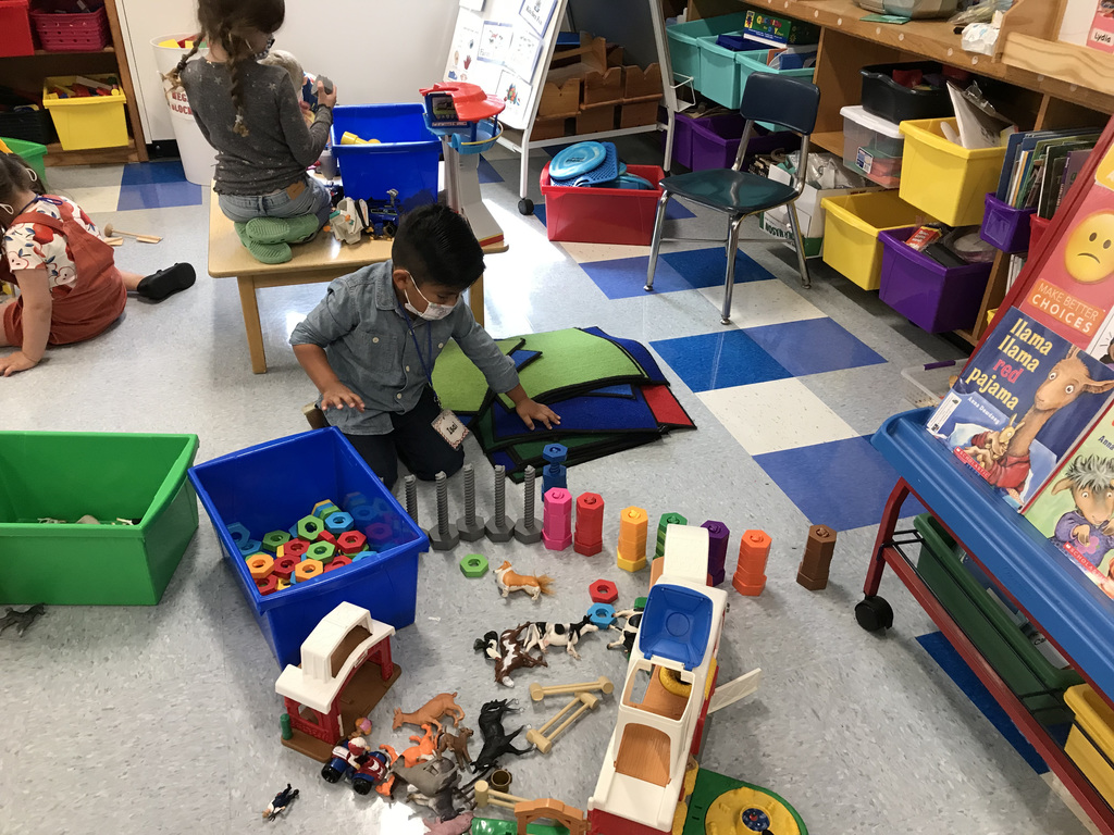 pre-kindergarten boy kneels on the classroom floor and plays with toys
