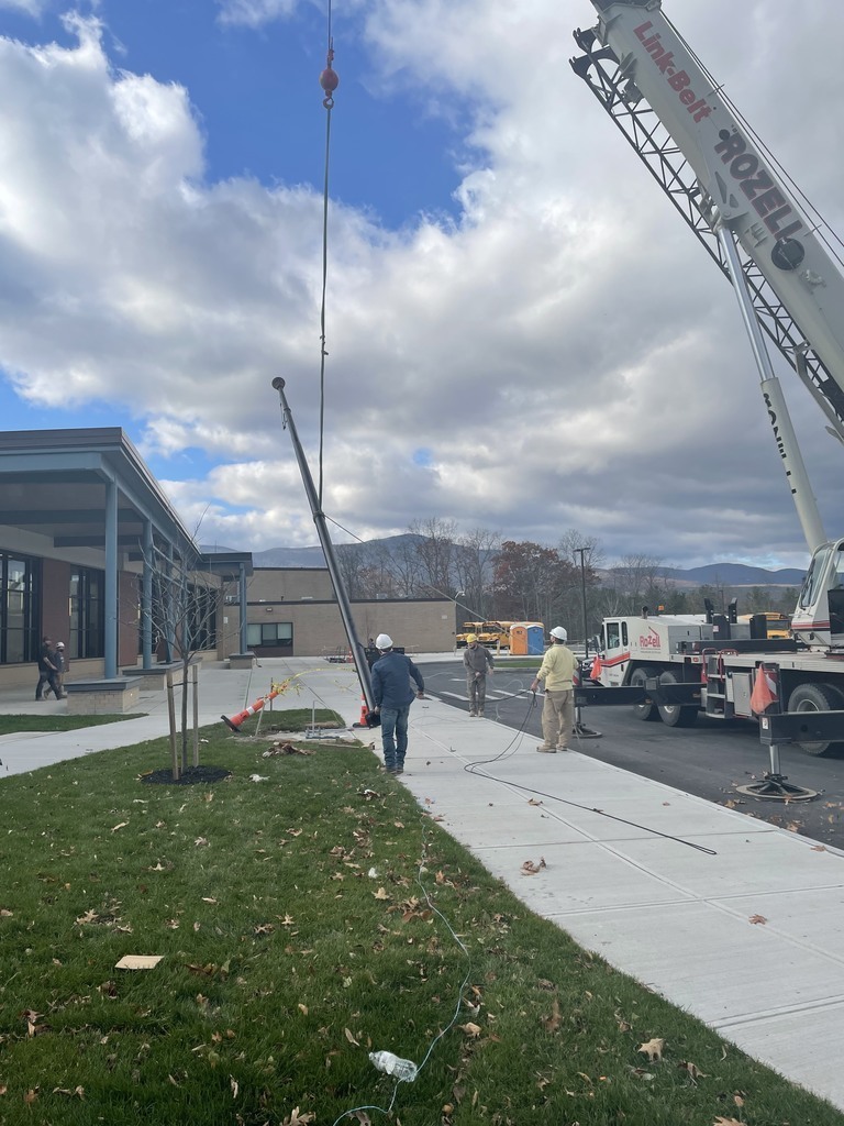 construction crews use a crane to install a flag pole in front of a school