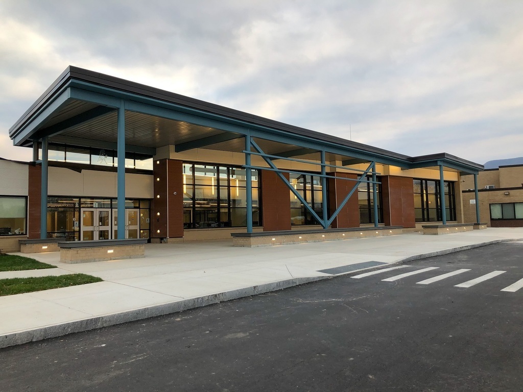 modern school entrance with and overhang, benches, large windows and teal posts