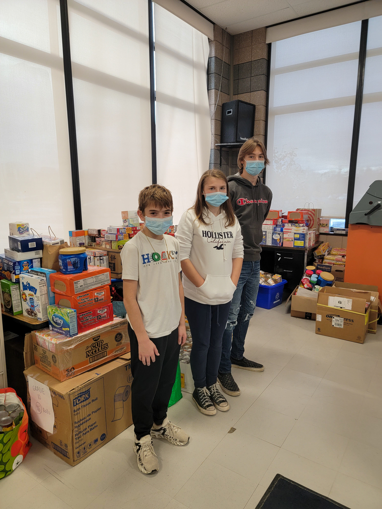 three students stand next to piles of non-perishable food items