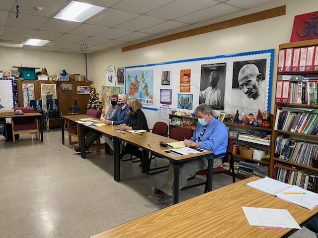a panel of four faculty judges sit at a table in the back of a classroom