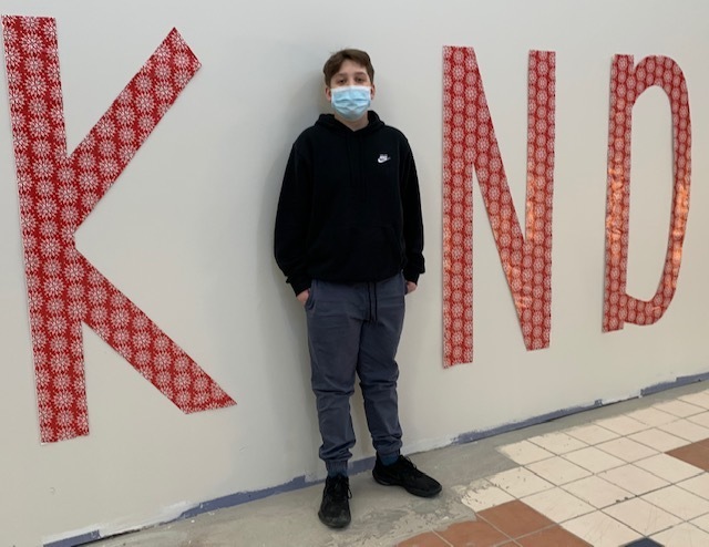 A student standing between the letters K, N, and D to spell out KIND
