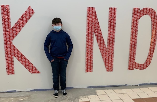 A student standing between the letters K, N, and D to spell out KIND