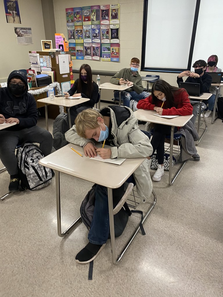 several high school students seated at desks writing and decorating cards