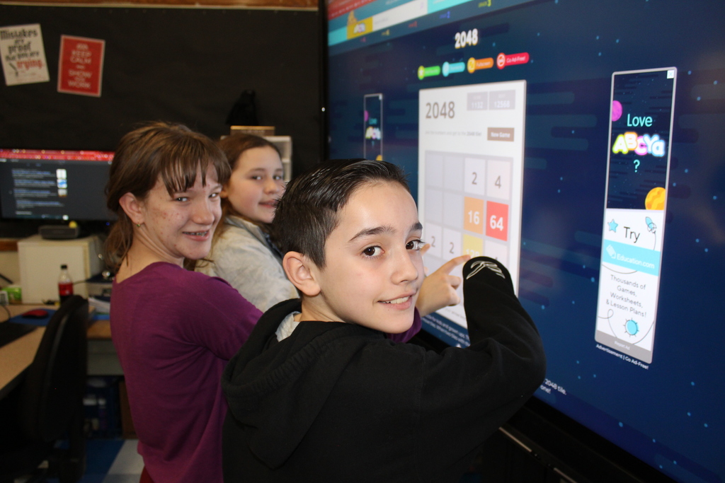 two girls and a boy touch the screen of an interactive whiteboard and play a number game