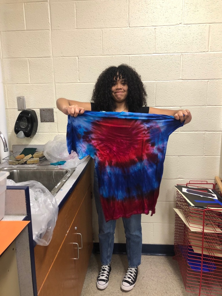 a female student holds up a red, purple and blue tie-dyed t-shirt at a sink