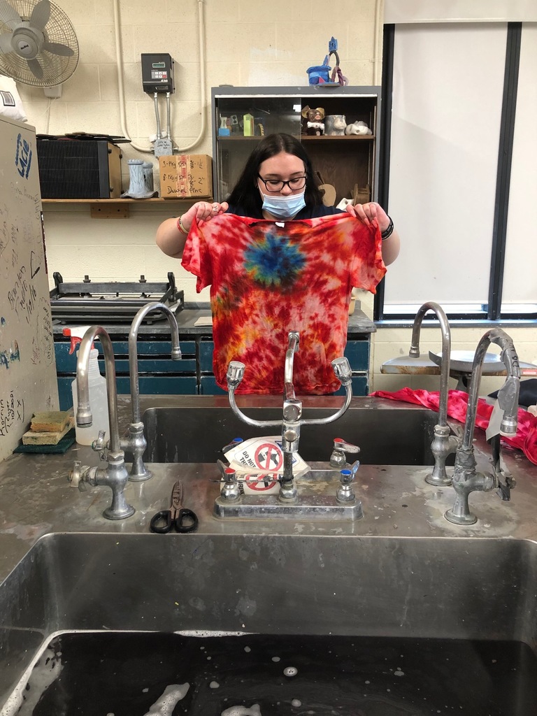 a female student holds up a red, orange and blue tie-dyed t-shirt at a sink
