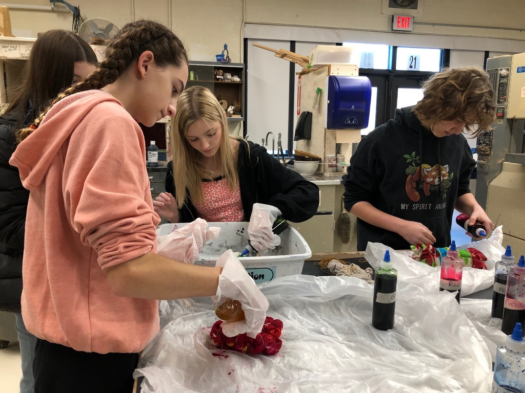 four students at an art work table wearing plastic gloves while they tie-dye shirts