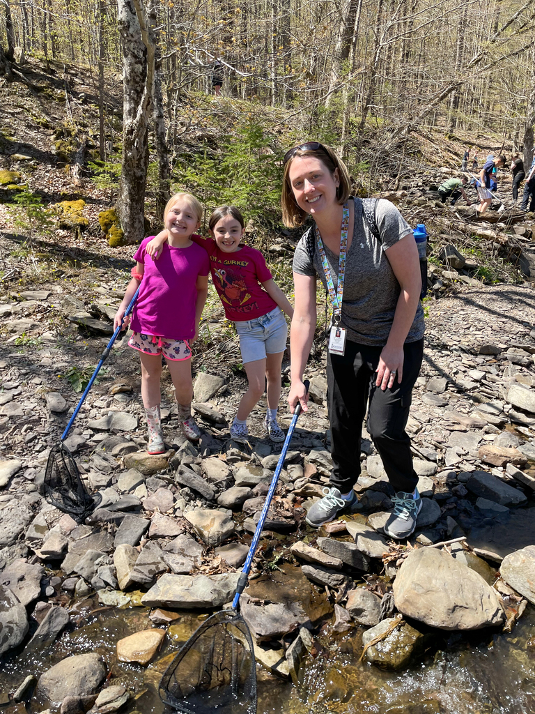 two elementary school girls and their female teacher outdoors on rocks at a nature preserve