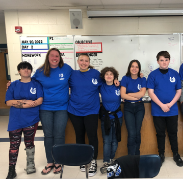 five middle school students and teachers wearing royal blue tshirts in the classroom