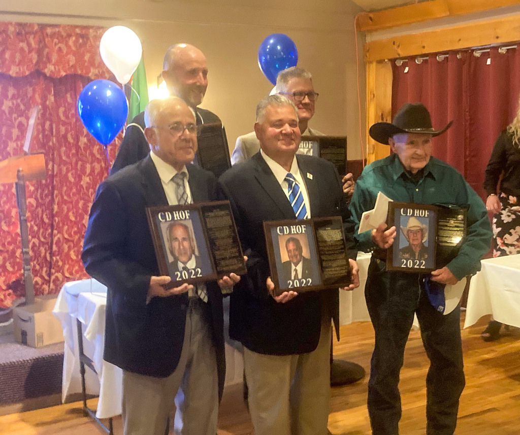 five elderly men wearing suits and ties holding plaques with blue and white balloons behind them