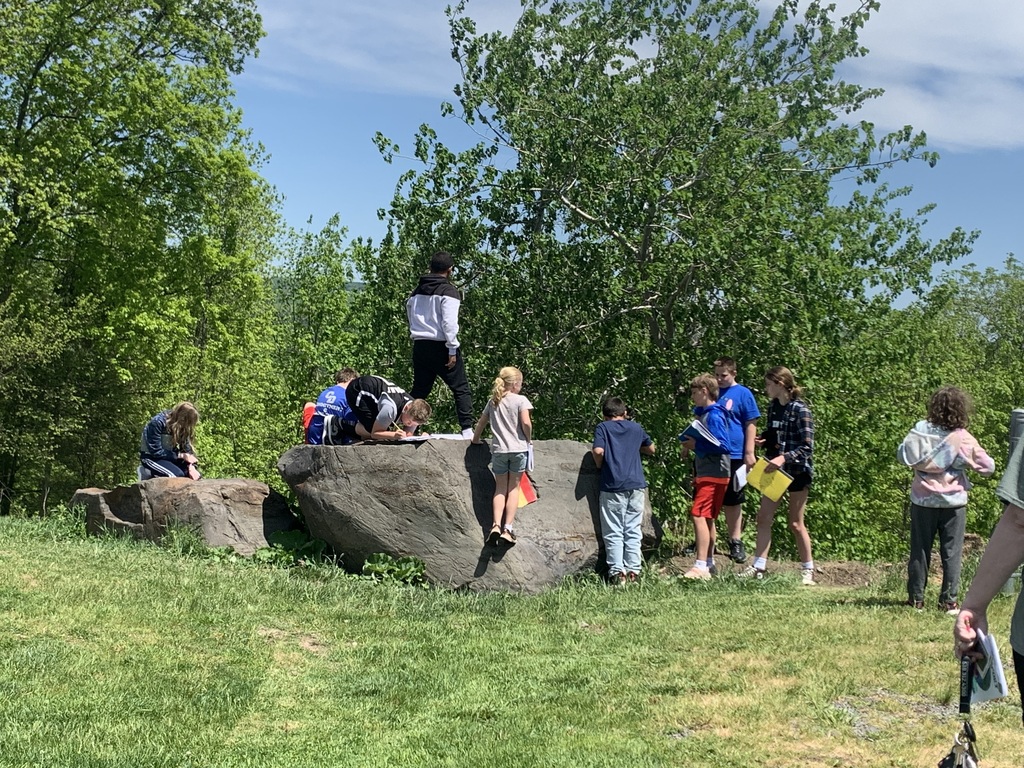 middle school students outside climbing on and examining a large boulder