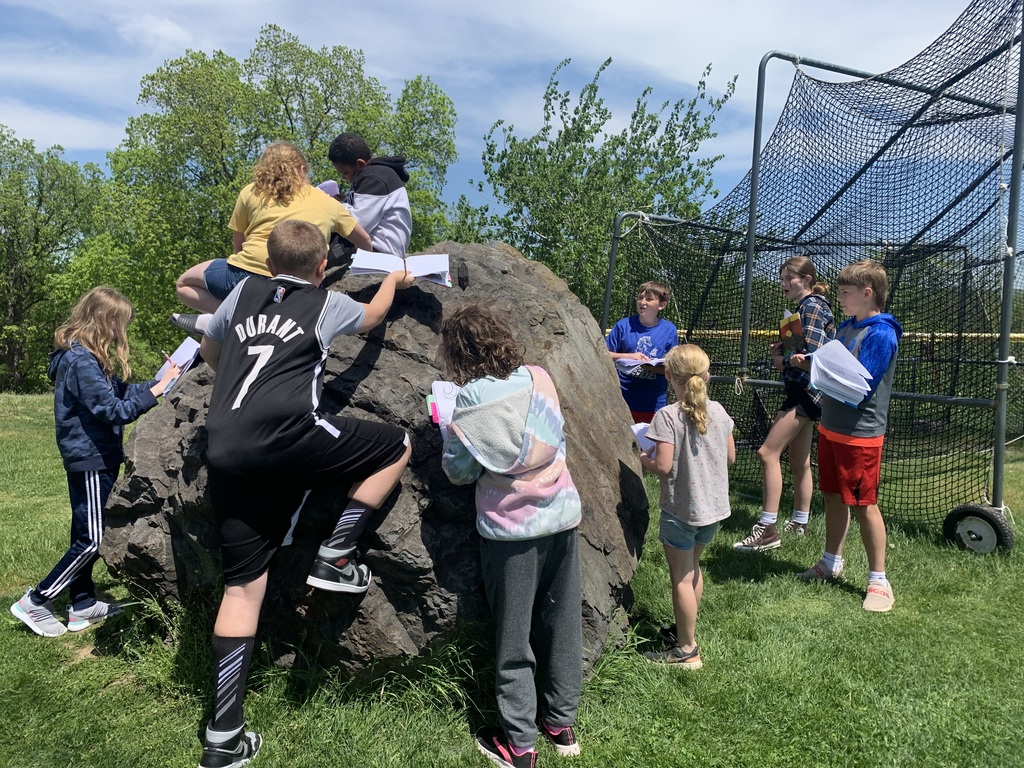 middle school students outside climbing on and examining a large boulder