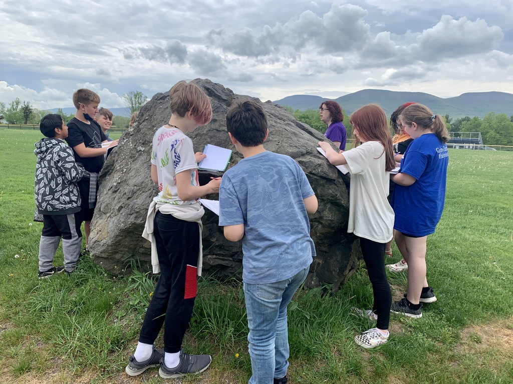 middle school students outside examining a large boulder