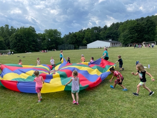 pre-kindergarten students playing outside with multicolored parachute