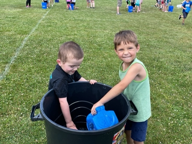 two pre-kindergarten boys and a bucket outdoors on the grass field